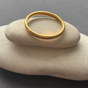 Op de afbeelding: Een eenvoudige, gladde, ronde gouden ring met een gepolijste afwerking. De ring heeft een consistent, afgerond profiel over de gehele omtrek en vertoont een heldere, reflecterende geelgouden tint die het licht gelijkmatig over het oppervlak vangt.
