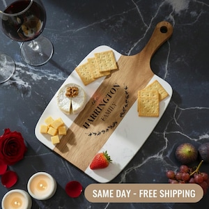 May include: A wooden and marble serving board with the text "the HARRINGTON FAMILY" and a decorative wreath. The board holds crackers, cheese, and a strawberry. A glass of red wine and candles are also present.