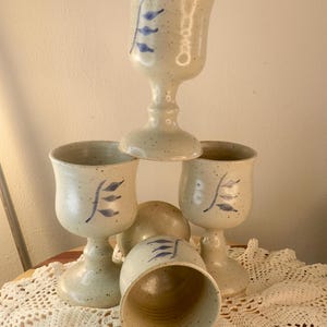 May include: Set of four ceramic goblets with a speckled glaze and blue leaf designs. The goblets are stacked on top of each other.