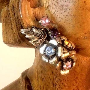 May include: A silver and gold tone earring with a cluster of colorful rhinestones and a leaf design.