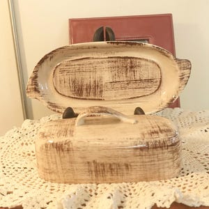 Peut inclure: Un beurrier en céramique avec un couvercle et une poignée. Le plat est décoré d'un motif vieilli brun et blanc.