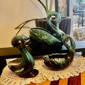 May include: A set of three ceramic figurines featuring a duck and two swans, all finished in a dark green and black drip glaze. The duck stands upright, while the two swans are depicted in varying sizes with curved necks and detailed wing textures.