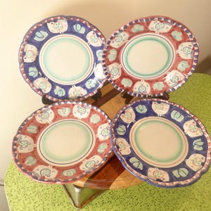 Peut inclure: Quatre assiettes décoratives en céramique aux bords festonnés. Deux assiettes ont une bordure bleue avec des motifs blancs et bleus, et deux ont une bordure rouge avec des motifs blancs et rouges. Chaque assiette a un centre vert clair.