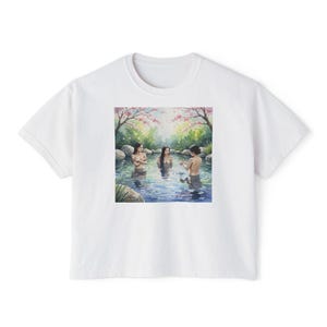 May include: White t-shirt with a watercolour illustration of three people in a natural hot spring. The artwork shows a serene scene with cherry blossom trees and rocks surrounding the water.