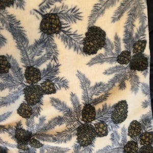 May include: White fleece fabric with a repeating pattern of blue pine branches and brown pine cones.