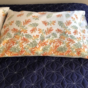 May include: Two white pillowcases with a pattern of orange, yellow, and green leaves on a navy blue quilted bedspread.