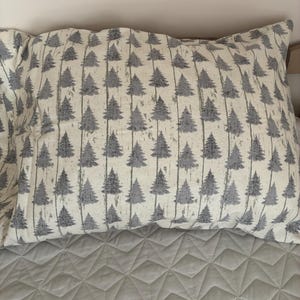 May include: A rectangular pillowcase featuring a repeating pattern of grey evergreen trees arranged in vertical rows against an off-white background. The fabric displays a textured appearance with thin vertical lines separating the tree motifs.
