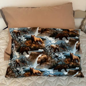 May include: A rectangular pillowcase featuring a repeating pattern of brown grizzly bears in a mountainous landscape with waterfalls and rocky terrain. The bears are depicted in various poses, walking and standing among the blue and white water.