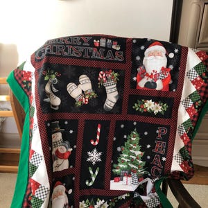 May include: A festive Christmas quilt with Santa Claus, snowmen, and seasonal motifs. The quilt has a black background with red check borders and the words "MERRY CHRISTMAS" and "PEACE".
