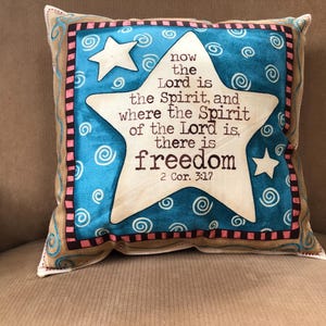 May include: Square decorative pillow with a blue and white star design. The pillow features the text "now the Lord is the Spirit, and where the Spirit of the Lord is, there is freedom" and is accented with white stars and swirls.