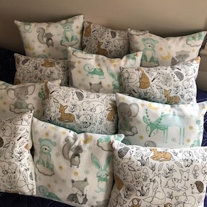 May include: A collection of throw pillows with woodland animal designs. The pillows feature illustrations of squirrels, foxes, rabbits, and deer in soft pastel colors. The pillows are arranged on a dark blue surface.