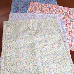 May include: Four fabric squares with a religious theme. The top square is light blue with a pattern of crosses. The second square is peach with a pattern of crosses. The third square is light blue with a pattern of crosses. The bottom square is light green with a pattern of words and phrases related to faith, love, and peace.