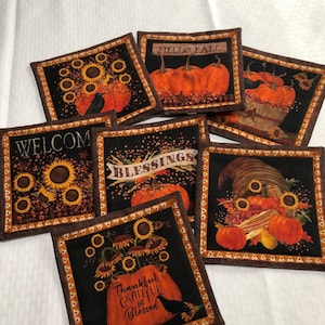 May include: Set of six black and brown fabric coasters with fall-themed designs. The coasters feature pumpkins, sunflowers, and the words "Welcome", "Blessings", "Hello Fall", and "Thankful Grateful and Blessed".