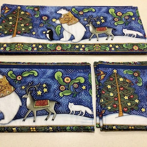 May include: Set of three blue and white fabric placemats with a winter holiday theme. The placemats feature a snowy scene with polar bears, reindeer, and a fox. The placemats have a blue background with white snowflakes and a border of green, red, and yellow.
