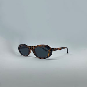 May include: Oval-shaped sunglasses with a tortoiseshell pattern frame and dark lenses.