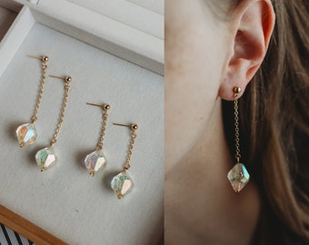 May include: A pair of gold dangle earrings with iridescent crystal teardrop charms. The earrings are shown on a white background and on a model's ear.