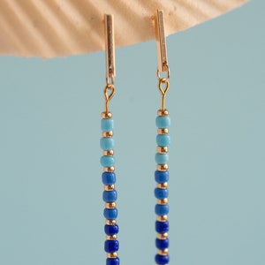 May include: A pair of gold dangle earrings with blue and turquoise beads. The beads are arranged in a gradient from dark blue to light turquoise.