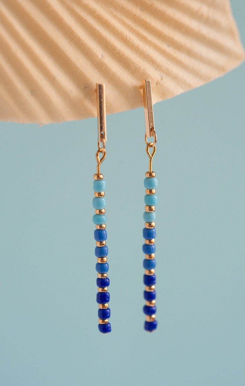 May include: A pair of gold dangle earrings with blue and turquoise beads. The beads are arranged in a gradient from dark blue to light turquoise.