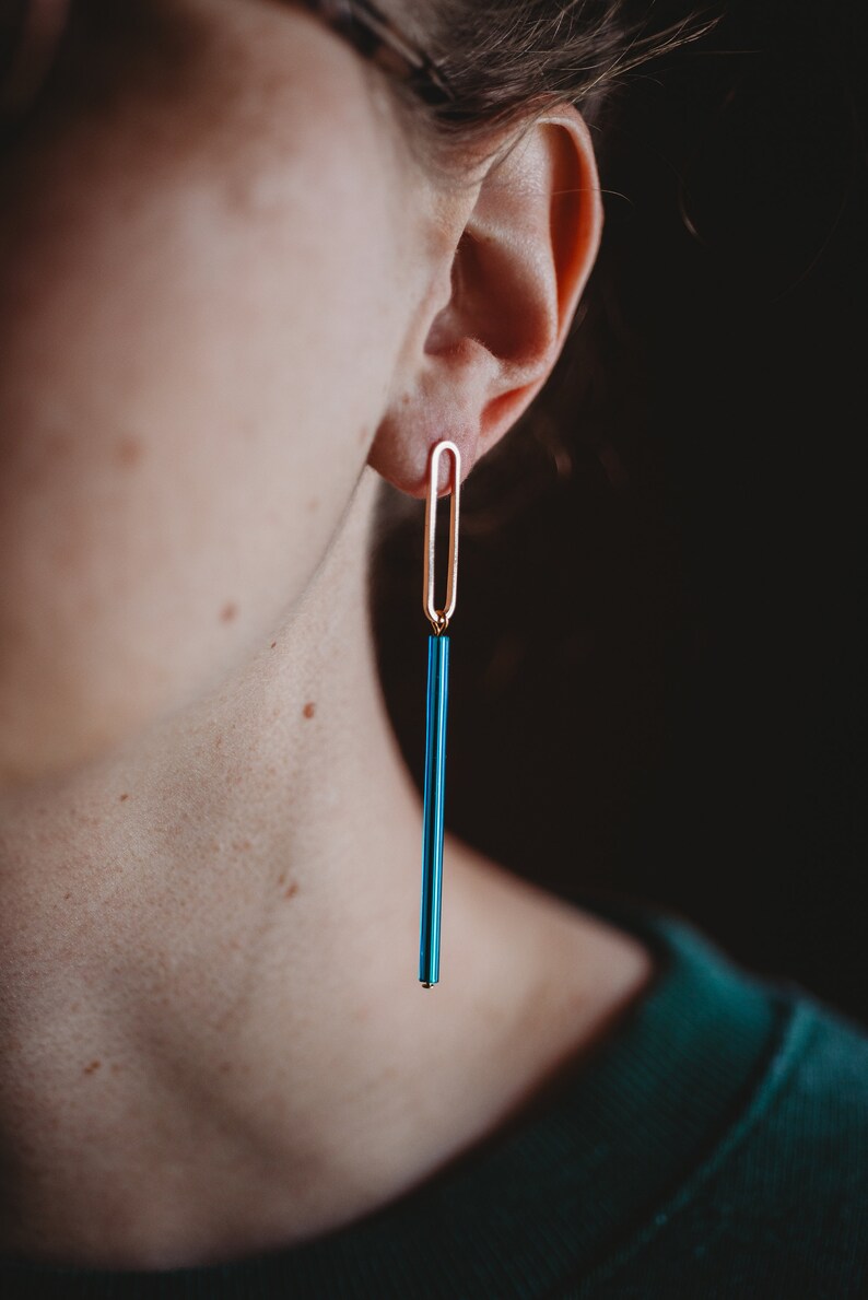 Peut inclure: Une paire de longues boucles d'oreilles bleues et dor&eacute;es. Les boucles d'oreilles sont compos&eacute;es d'une tige bleue fine avec une boucle dor&eacute;e en haut.