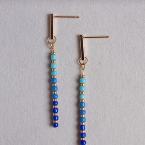May include: A pair of gold dangle earrings with a gradient of blue and turquoise beads.