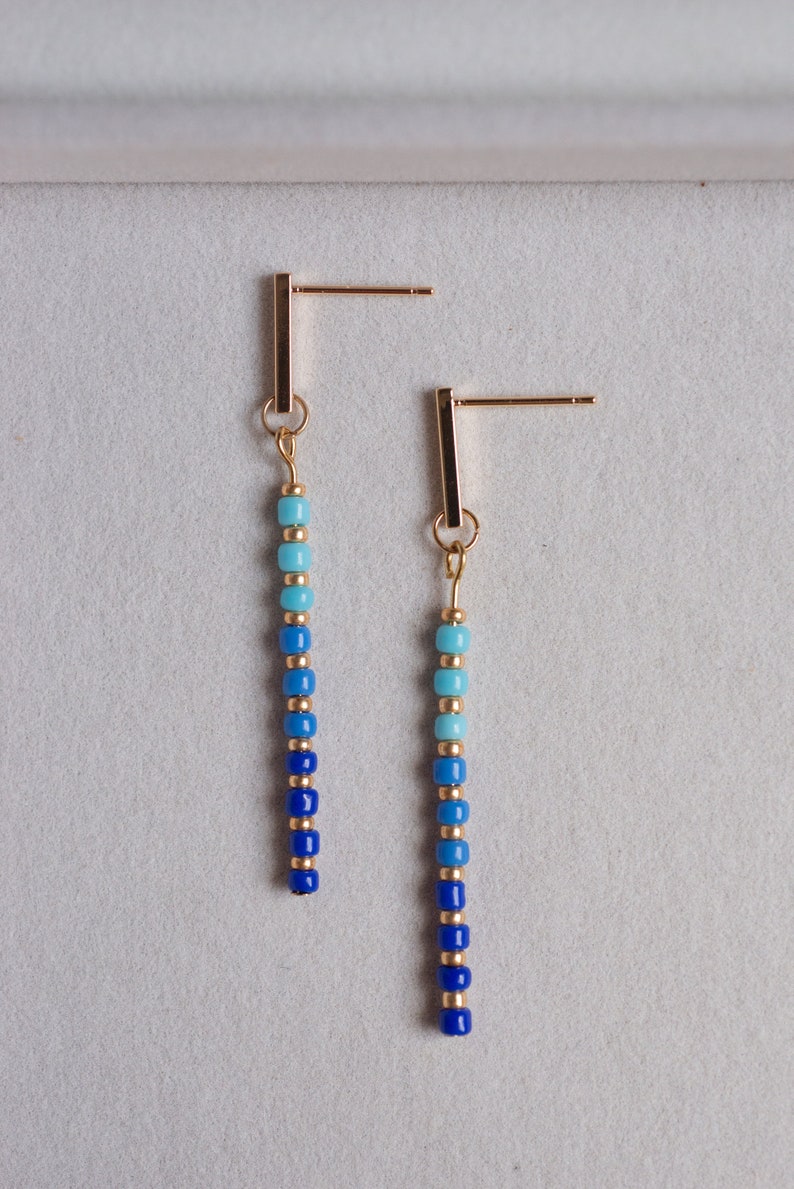 May include: A pair of gold dangle earrings with a gradient of blue and turquoise beads.