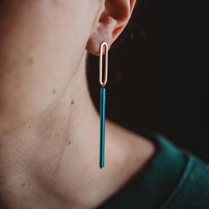Peut inclure: Une paire de boucles d'oreilles longues et pendantes avec un dessus ovale dor&eacute; et un bas rectangulaire bleu sarcelle.