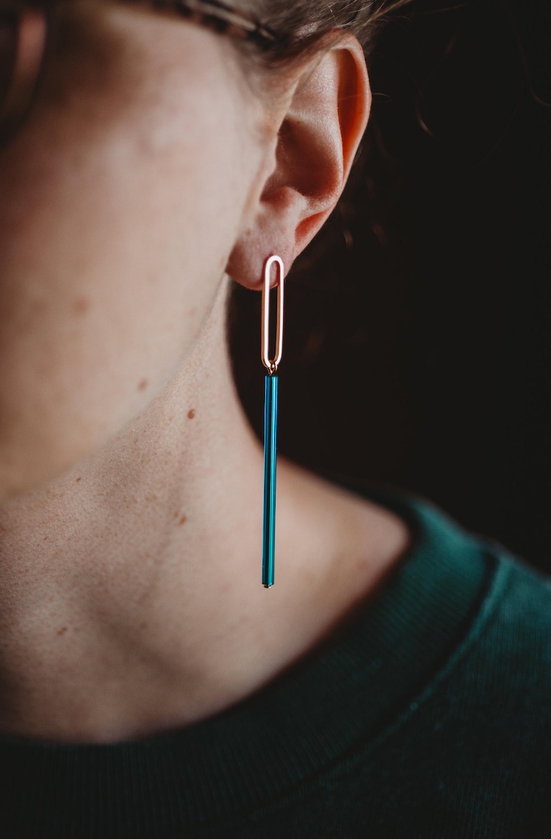 Peut inclure: Une paire de boucles d'oreilles longues et pendantes avec un dessus ovale dor&eacute; et un bas rectangulaire bleu sarcelle.