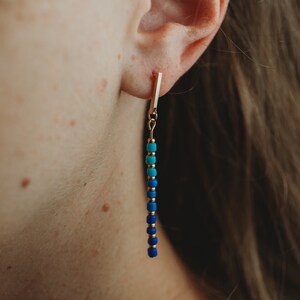 May include: Gold bar earrings with a blue and turquoise beaded chain.