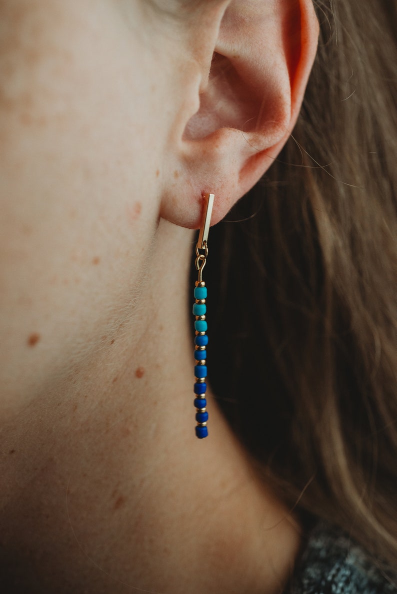 May include: Gold bar earrings with a blue and turquoise beaded chain.