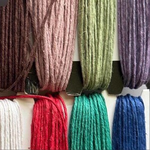 May include: Close-up of a selection of colorful twine spools. The spools display a range of colors, including brown, pink, green, purple, white, red, teal, and blue. The twine is tightly wound and appears to be made of natural fibers.