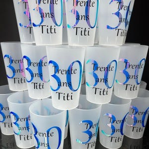 Może przedstawiać: Kolekcja mrożonych plastikowych kubków. Każdy kubek jest ozdobiony liczbą "30", słowem "Trente", słowem "ans" i imieniem "Titi" w niebieskiej i opalizującej czcionce. Kubki są ułożone jeden na drugim.