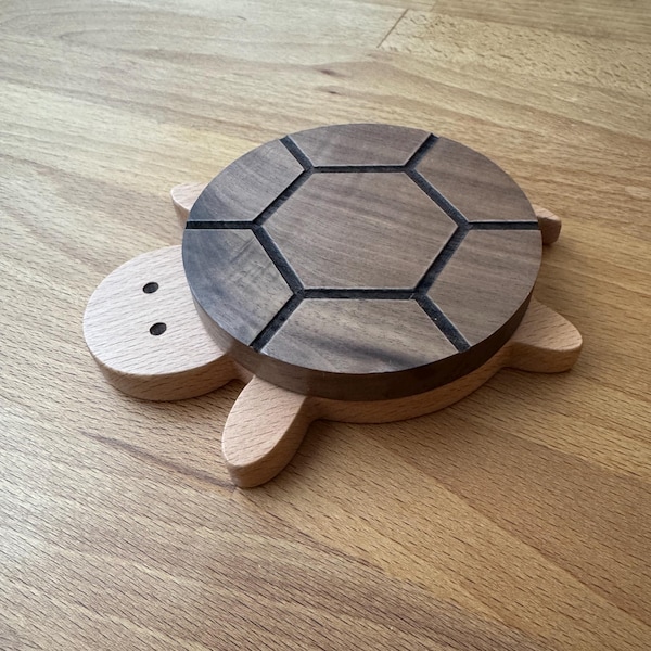 May include: A wooden turtle shaped coaster with a dark brown walnut top and a light brown base. The top has a hexagonal pattern carved into it.