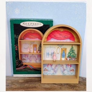May include: A tan-colored Keepsake Ornament shelf with a miniature stage design featuring a ballerina, Christmas tree, and the words "The Nutcracker Ballet." The ornament is in its original box, which has a green and red design.