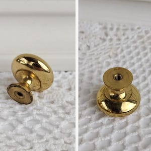 Op de afbeelding: Twee aanzichten van een goudkleurige kastknop. De knop heeft een afgeronde bovenkant en een korte, cilindrische basis. Het metaal heeft een glanzende afwerking. De knop is ontworpen voor meubels en woondecoratie.