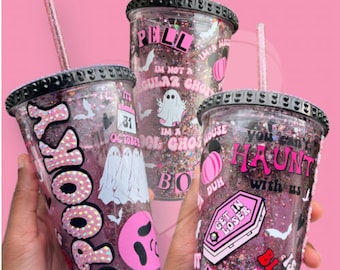 May include: Three Halloween-themed tumblers with pink and black accents. Each tumbler features glitter, decorative stickers, and text including "Spooky", "Haunt", and "Get in Loser". The tumblers have black lids and pink straws.