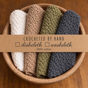 Könnte beinhalten: Vier gefaltete Baumwolltücher in Weiß, Beige, Olivgrün und Anthrazit mit einer strukturierten Häkelmasche. Ein Papierband in der Mitte trägt die Aufschrift: CROCHETED BY HAND, dishcloth, washcloth, 100% cotton.