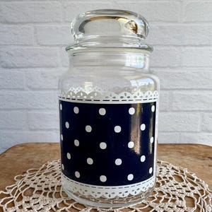 May include: A clear glass jar with a white lace trim and a black and white polka dot design. The jar has a lid.