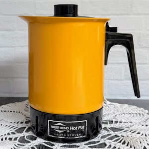 May include: A vintage West Bend Hot Pot, with a vibrant yellow body and black base, handle, and lid. The appliance has a Heat & Serve function, as indicated by the text on the front. This electric coffee pot is a retro kitchen appliance.