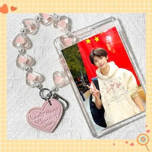 Pode incluir: Capa de telefone transparente com foto de uma pessoa. A capa tem um pingente em forma de coração rosa e uma etiqueta em forma de coração correspondente que diz "Lovely Home Sweet Love".
