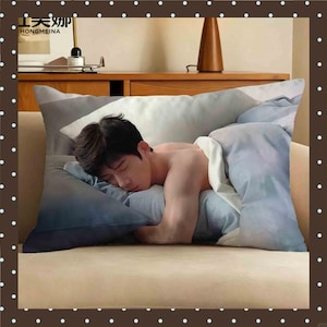 May include: A rectangular throw pillow featuring a photographic print of a person with dark hair sleeping peacefully while tucked under light blue and white bedding. The pillow displays a realistic image of a person resting their head on a pillow.