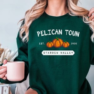 May include: Green sweatshirt with a white graphic that says "Pelican Town Est. 2016 Stardew Valley" with a pixelated image of pumpkins.