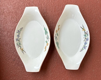 May include: Two white oval ceramic baking dishes with floral designs. The dishes have brown rims and feature a pattern of blue, yellow, and green flowers.