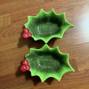 Puede incluir: Dos platos de servir de cerámica verde en forma de hoja de acebo con bayas rojas.