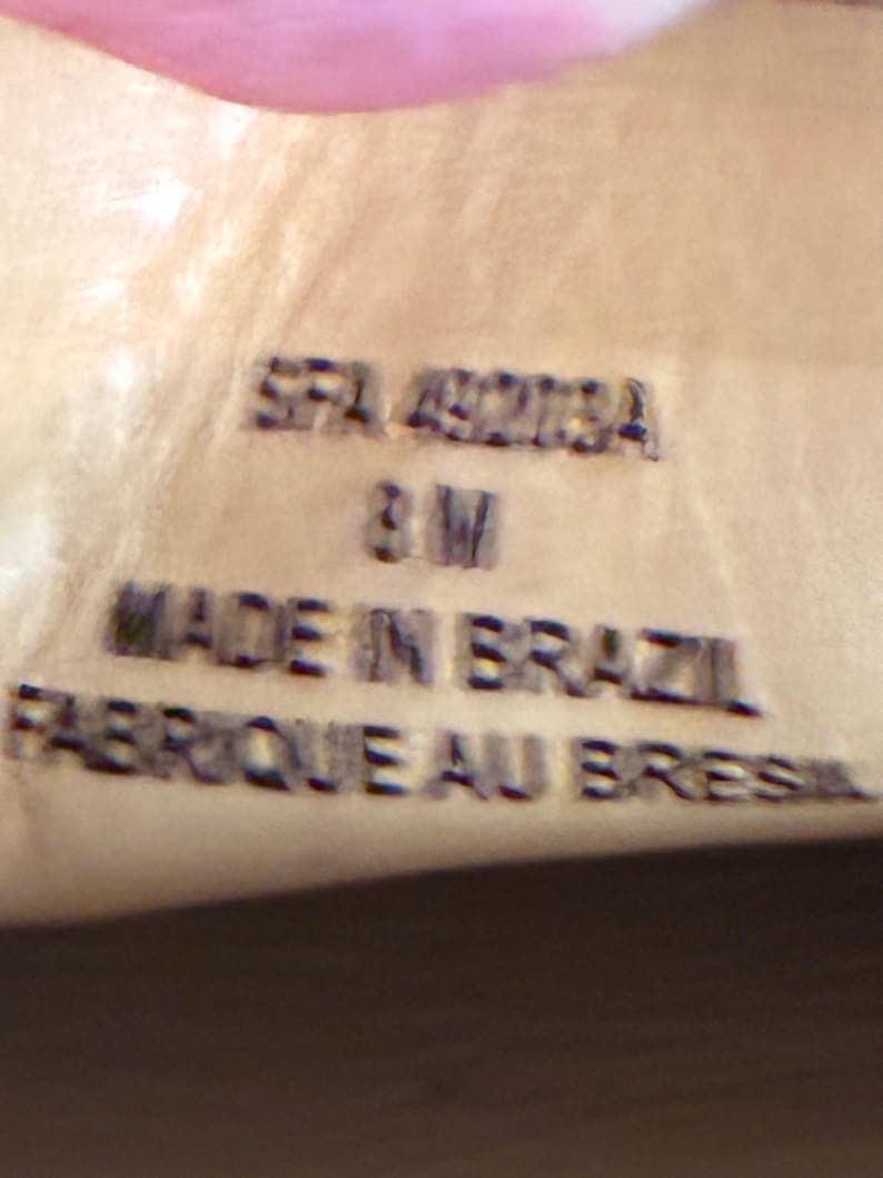 May include: A light tan leather surface featuring embossed black text that reads SFA 49218A, 8 M, MADE IN BRAZIL, and FABRIQUE AU BRESIL. The lettering is clearly stamped into the material, providing product information in a clear, legible font style.