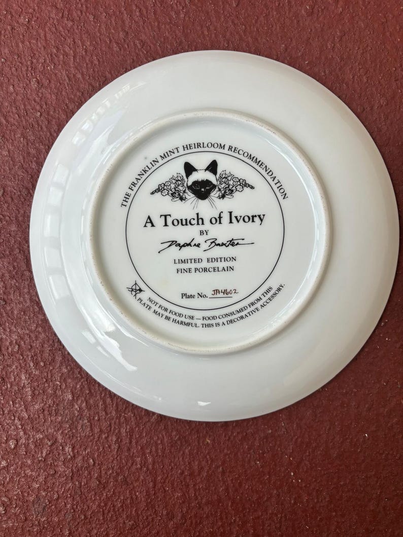May include: White porcelain plate with a black and white cat illustration and the text "A Touch of Ivory" by Daphne Baxter. The plate is a limited edition fine porcelain piece, plate number JA4602.
