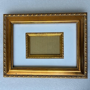 May include: A rectangular gold picture frame with a smaller gold frame inside. The frame has a white matting and a decorative beaded edge. The inner frame has a tan background.
