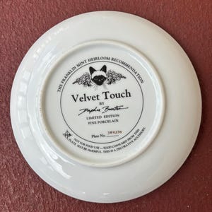 May include: A white porcelain plate with a black and white cat illustration in the center. The plate has text that reads "Velvet Touch" and "Limited Edition Fine Porcelain". The plate is a decorative accessory.