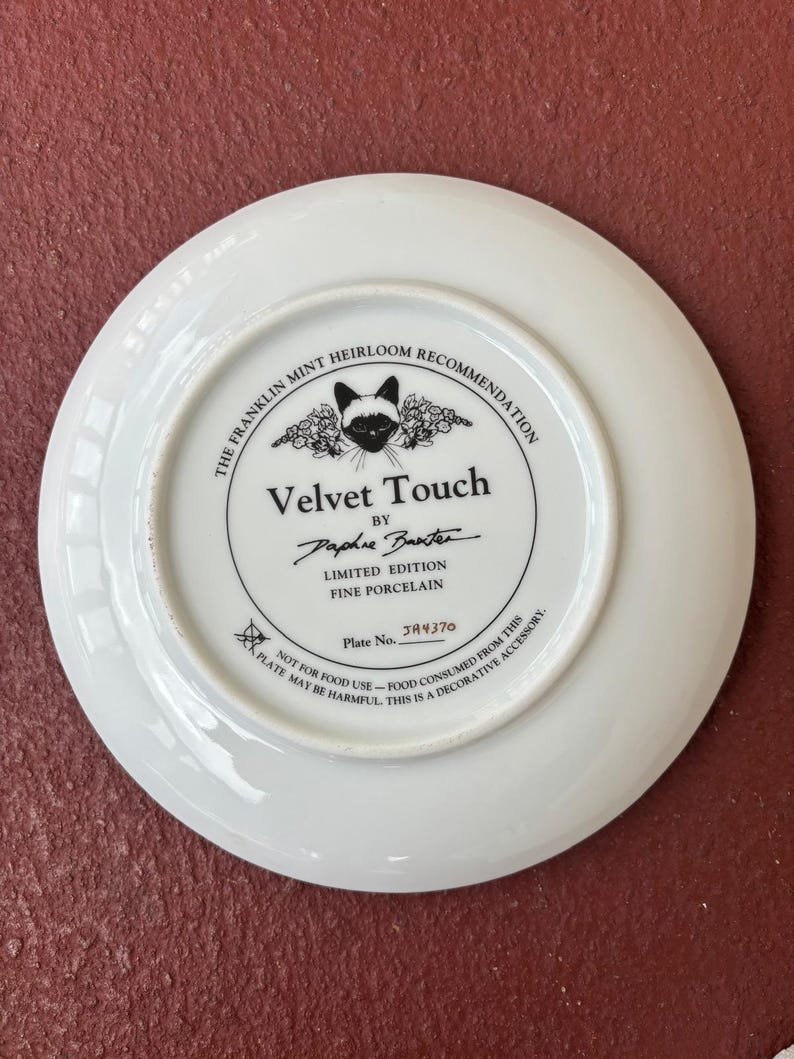 May include: A white porcelain plate with a black and white cat illustration in the center. The plate has text that reads "Velvet Touch" and "Limited Edition Fine Porcelain". The plate is a decorative accessory.
