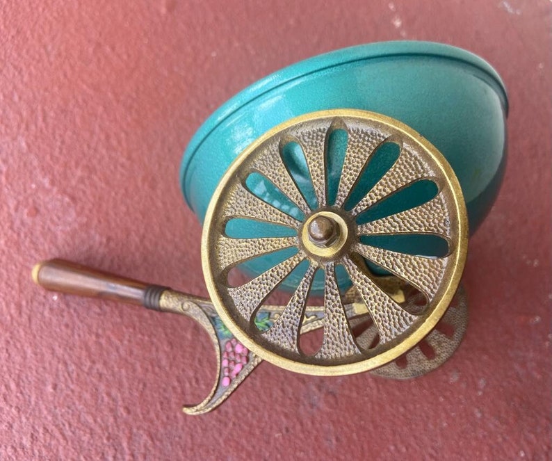 K&ouml;nnte beinhalten: Ein vintage Deko-Wagen in T&uuml;rkis und Messing mit einem Blumendesign am Griff. Der Wagen hat eine runde Schale und ein einzelnes Rad.