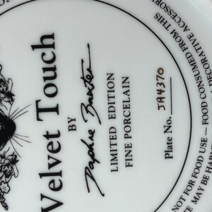 May include: White porcelain plate with a black and white Siamese cat illustration and floral accents. The plate is labeled "Velvet Touch" by Daphne Baxter, a limited edition fine porcelain piece. Plate number JA4370.